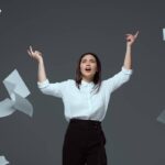 emotional young businesswoman throwing papers isolated on grey