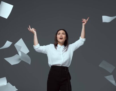 emotional young businesswoman throwing papers isolated on grey