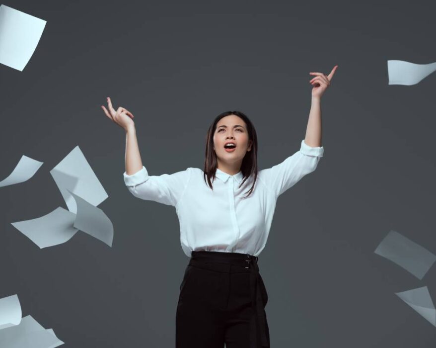 emotional young businesswoman throwing papers isolated on grey