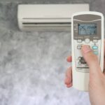 hand holding remote in front of air conditioner 2023 11 27 05 03 07 utc