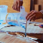 Closeup of carpenter pouring liquid epoxy in a wooden table