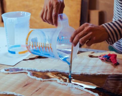 Closeup of carpenter pouring liquid epoxy in a wooden table