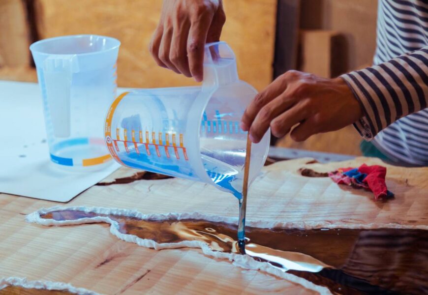 Closeup of carpenter pouring liquid epoxy in a wooden table
