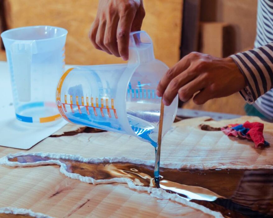 Closeup of carpenter pouring liquid epoxy in a wooden table