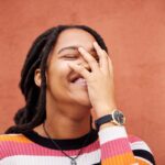 Happy, laughter and freedom with a black woman on an orange background outdoor for joy or humor. Fu