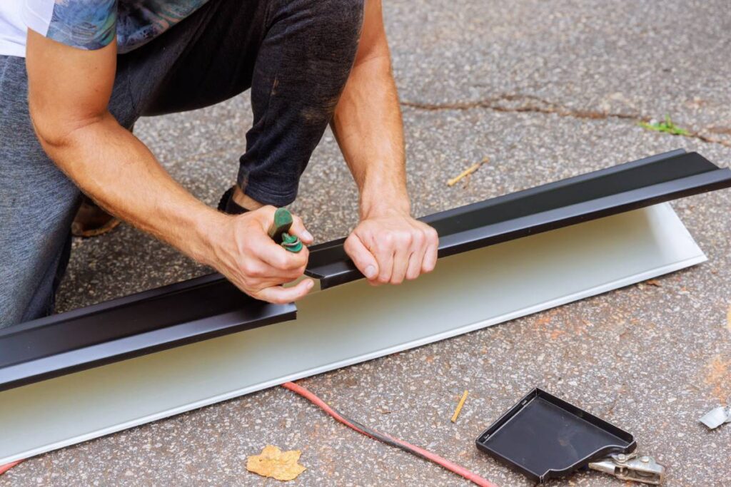 Worker cuts aluminum rain gutters to required size after bending them using a machine tool