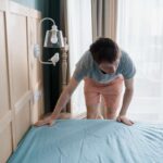 Adult man is putting the bedding cover or mattress pad on the bed. Regular bed linen change