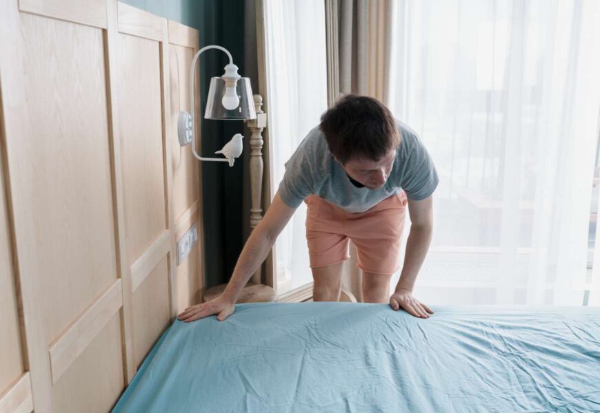 Adult man is putting the bedding cover or mattress pad on the bed. Regular bed linen change