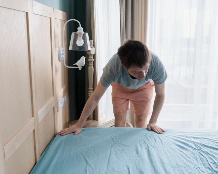 Adult man is putting the bedding cover or mattress pad on the bed. Regular bed linen change