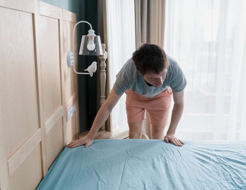 Adult man is putting the bedding cover or mattress pad on the bed. Regular bed linen change